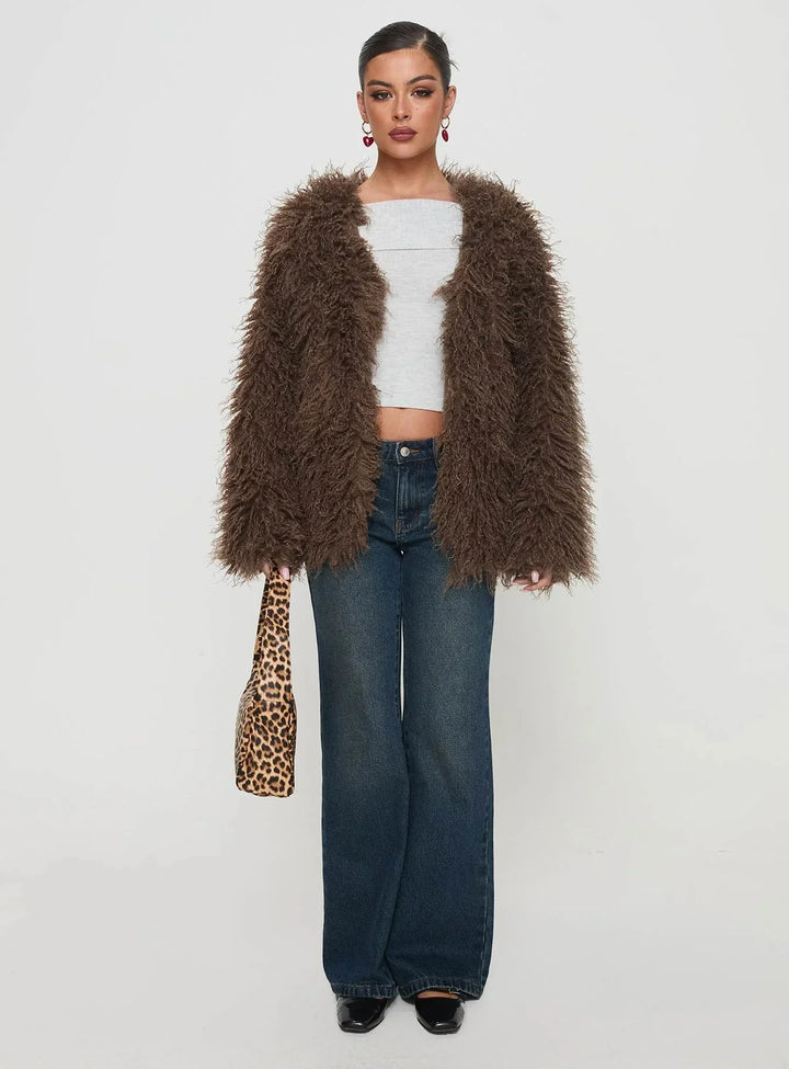 Woman wearing a brown fluffy jacket, white crop top, wide-leg jeans, black shoes, and holding leopard print handbag