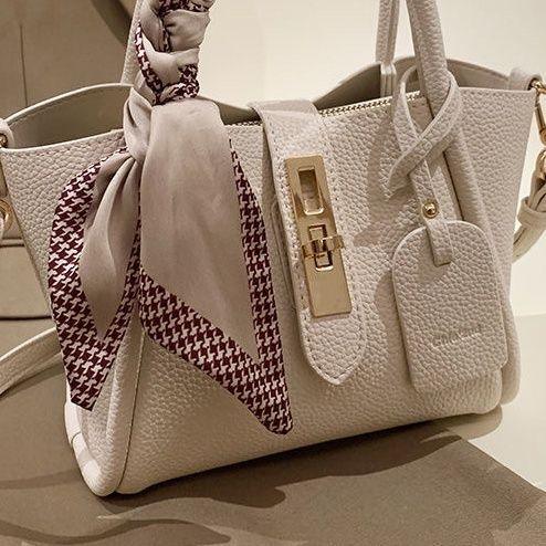 Cream textured leather handbag with gold clasp and beige patterned silk scarf tied on handle