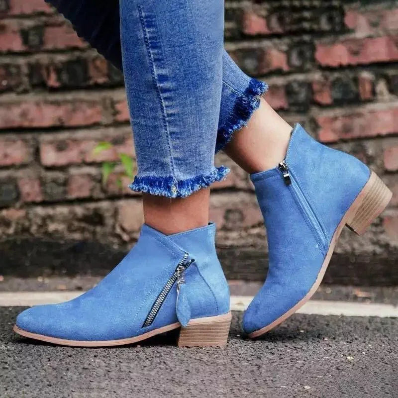 Women wearing light blue suede ankle boots with side zippers and frayed hem skinny jeans on pavement