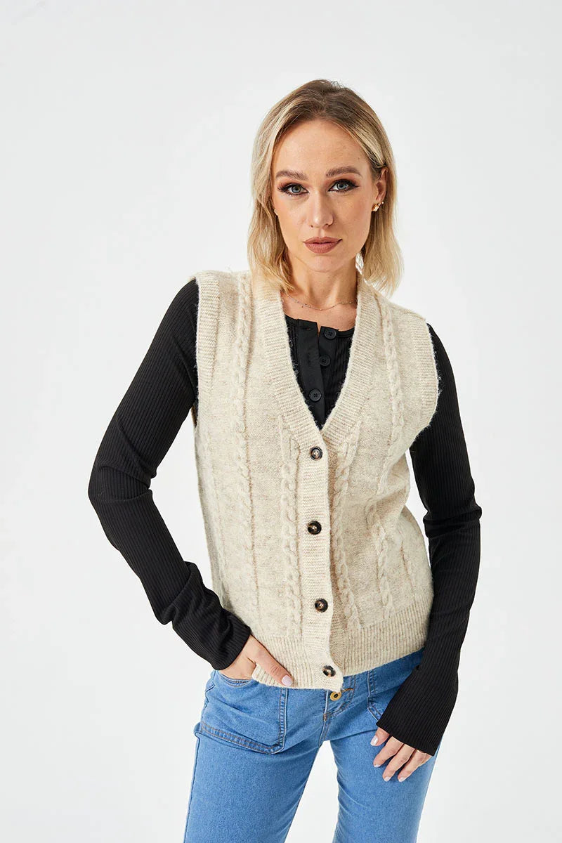 Blonde woman wearing cream knit button-up vest over black long sleeve top and blue jeans