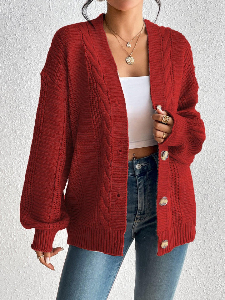 Woman wearing a red cable knit cardigan over a white crop top and blue jeans, styled with gold jewelry