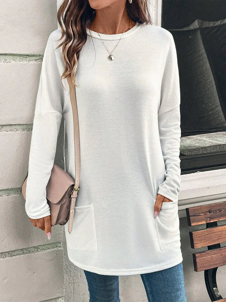 Woman wearing white long sleeve tunic sweater with pockets, blue jeans, and crossbody bag