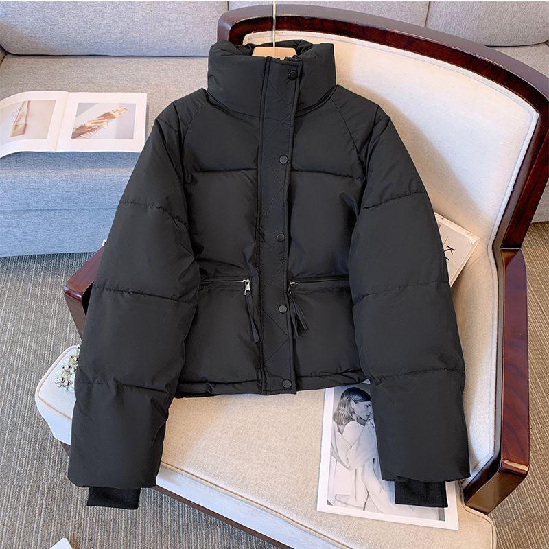 Black puffer jacket with high collar and zippered pockets displayed on beige armchair