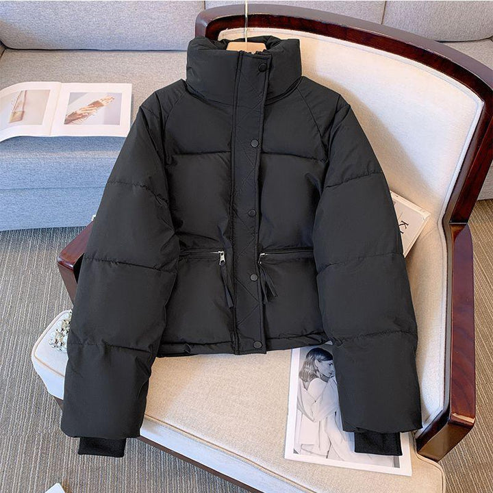 Black puffer jacket with high collar and zippered pockets displayed on beige armchair