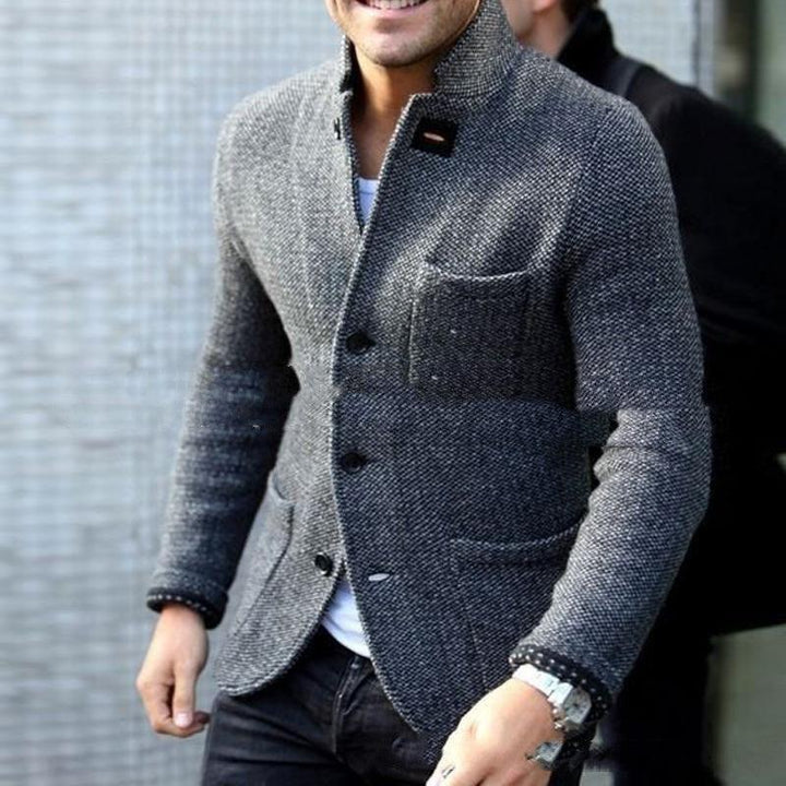 Man wearing a grey textured blazer with black buttons, white shirt, black jeans, and a wristwatch