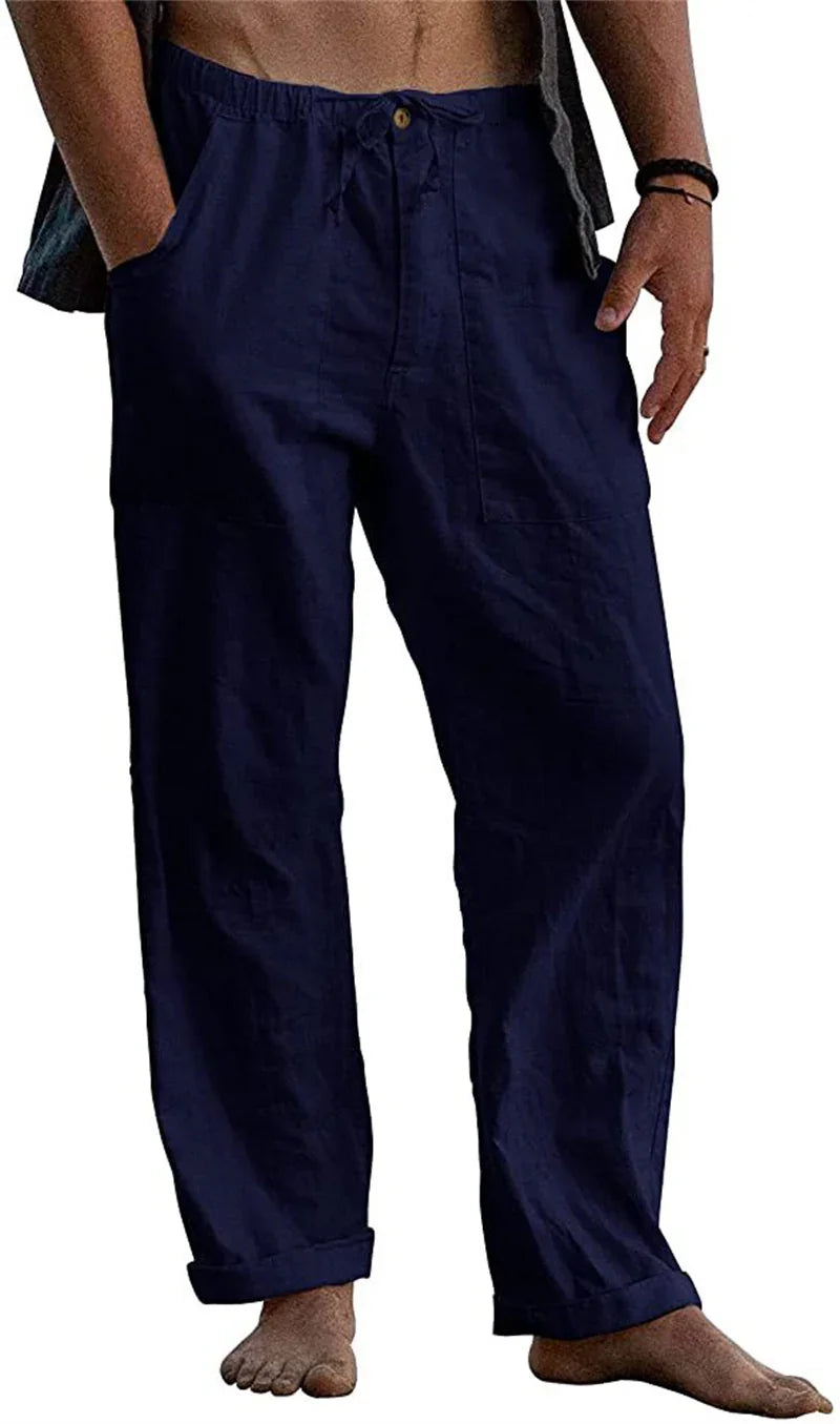 Man wearing loose navy blue casual pants with rolled cuffs, bare feet, and hands in pockets