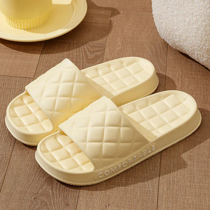 Yellow cushioned quilted slides slippers on wooden floor with soft texture and COMFORTABLE text