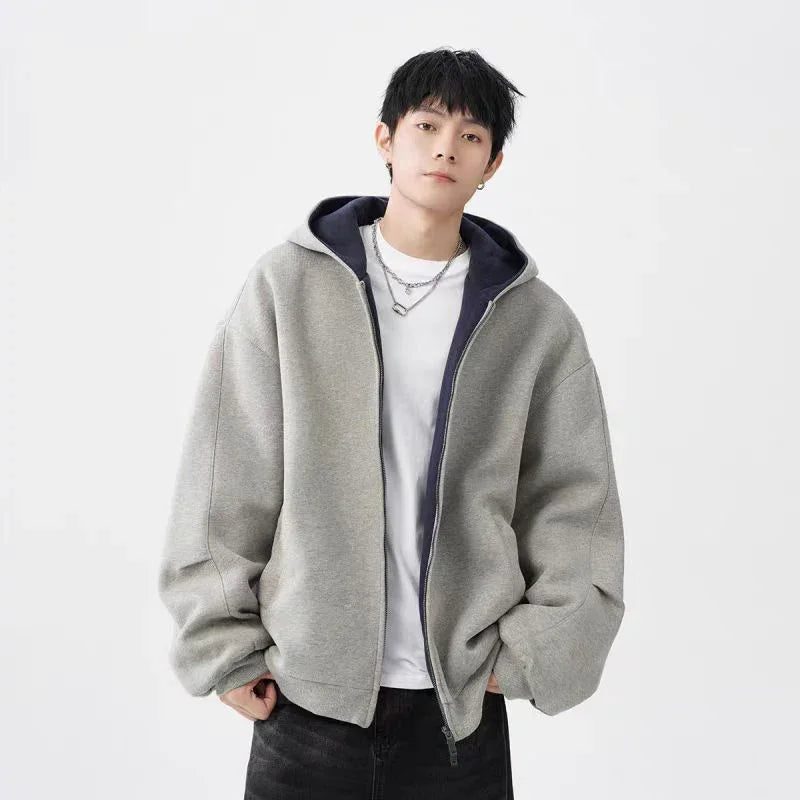 Young man wearing oversized gray zip-up hoodie with black lining and white t-shirt posing against white background