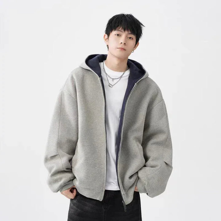 Young man wearing oversized gray zip-up hoodie with black lining and white t-shirt posing against white background