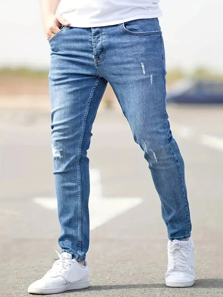 Man wearing slim fit blue distressed jeans and white sneakers standing outdoors