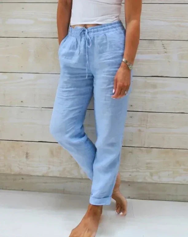 Woman wearing light blue linen drawstring pants and white cropped top against wooden wall