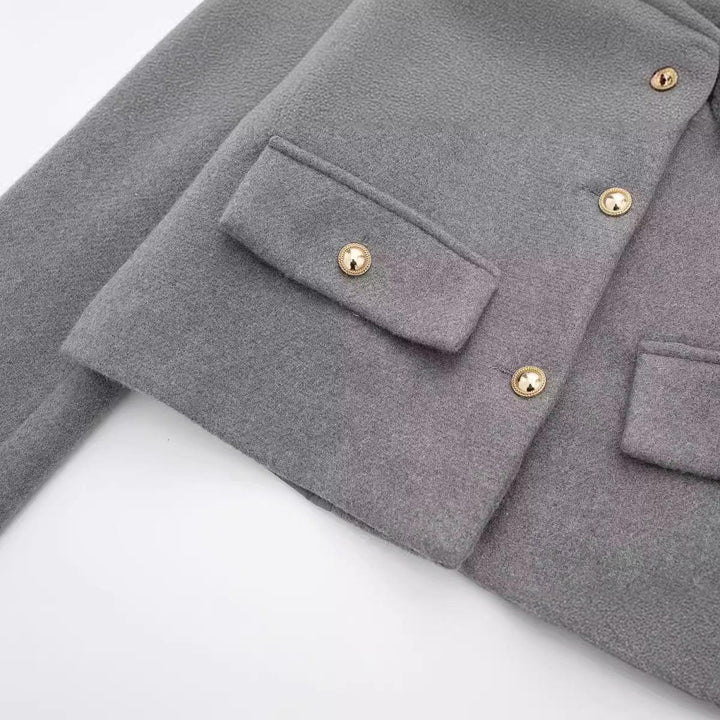 Close-up of gray wool coat with gold button details and flap pocket on white background