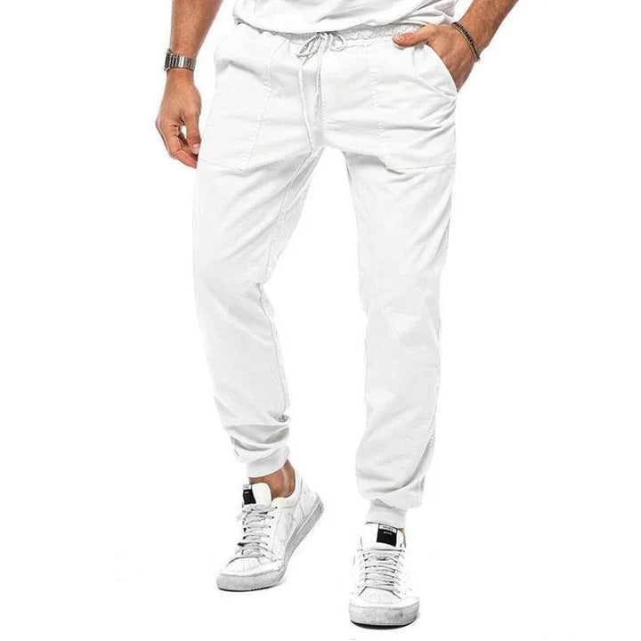 Men's white casual jogger pants with drawstring waist and white sneakers on white background