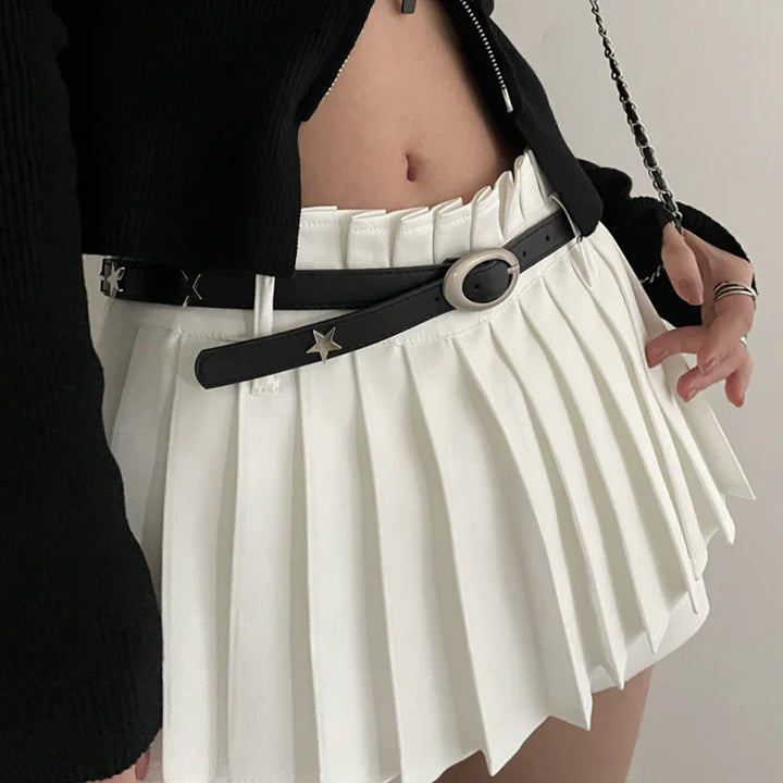 Close-up of woman wearing white pleated mini skirt with black star-studded belt and black cropped sweater