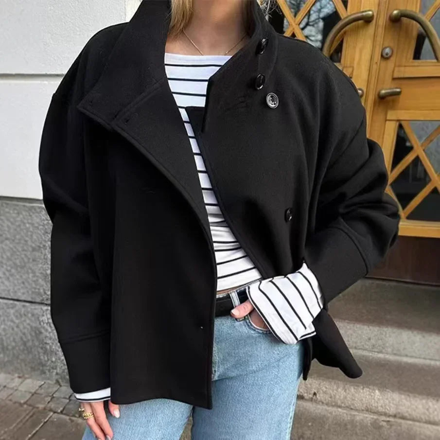 Woman wearing oversized black buttoned jacket over striped long sleeve top and light blue jeans outdoors