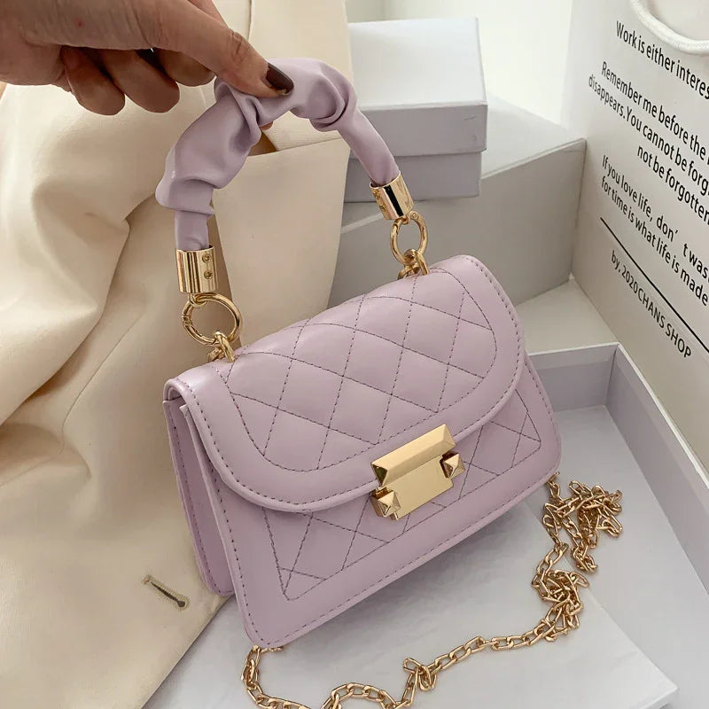 Light purple quilted leather handbag with gold clasp and chain, held by ruched handle