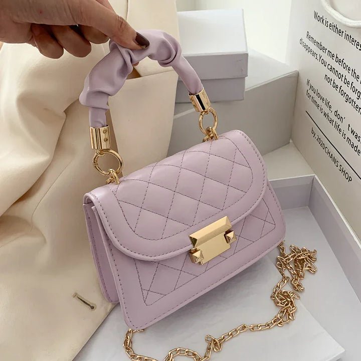 Light purple quilted leather handbag with gold clasp and chain, held by ruched handle
