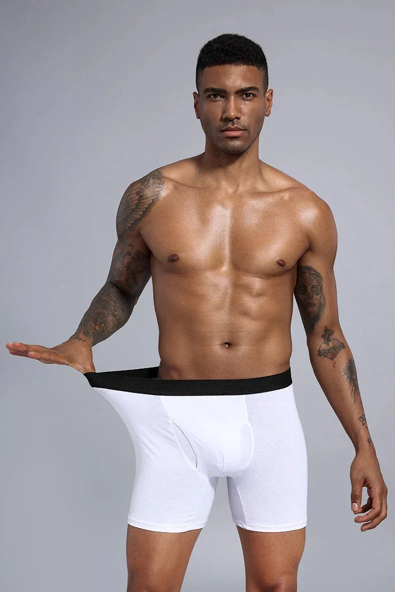 Fit shirtless man with tattoos stretching the waistband of loose white boxer briefs against gray background