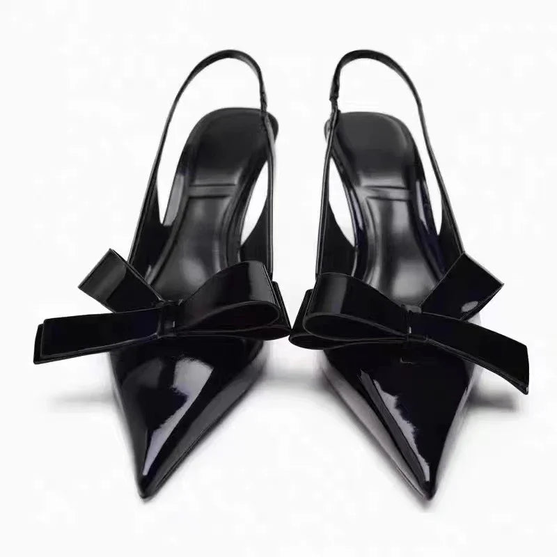 Black patent leather slingback heels with pointed toes and large bow detail on each shoe