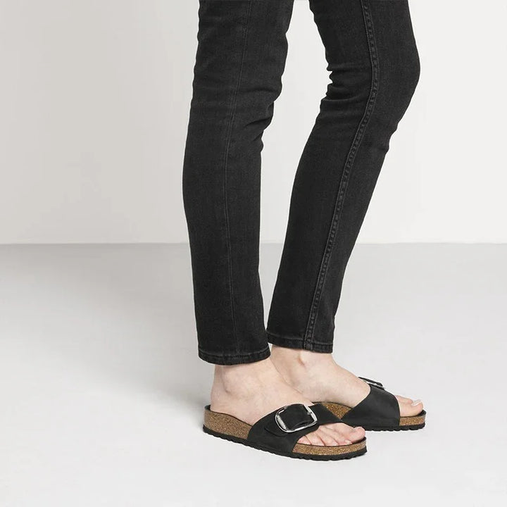 Person wearing black slim jeans and black cork sole slide sandals with large buckle detail