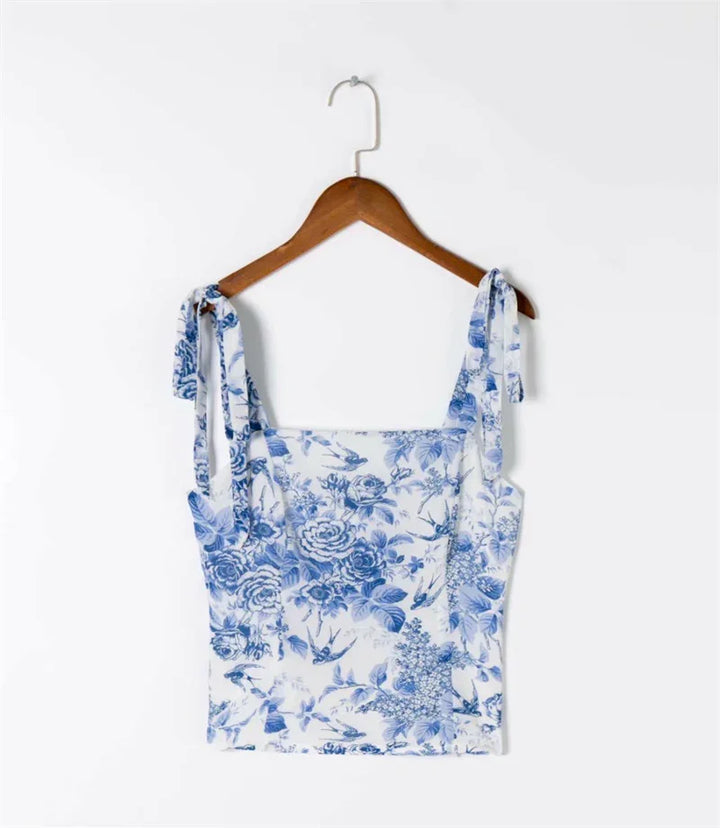 White crop top with blue floral and bird print, tied shoulder straps on wooden hanger