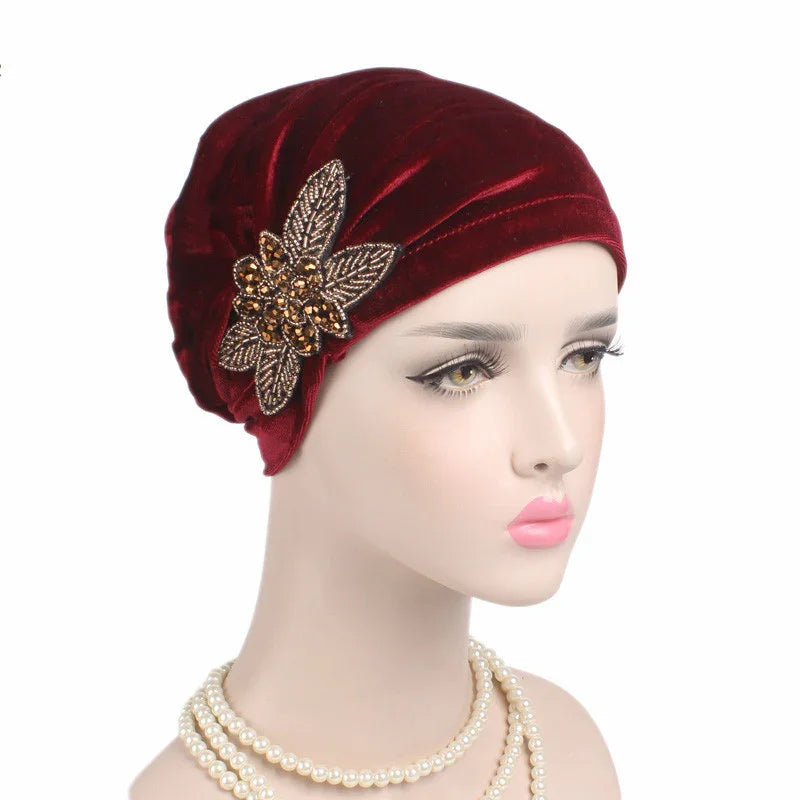 Mannequin wearing a deep red velvet turban with a gold embellished floral accessory and pearl necklace
