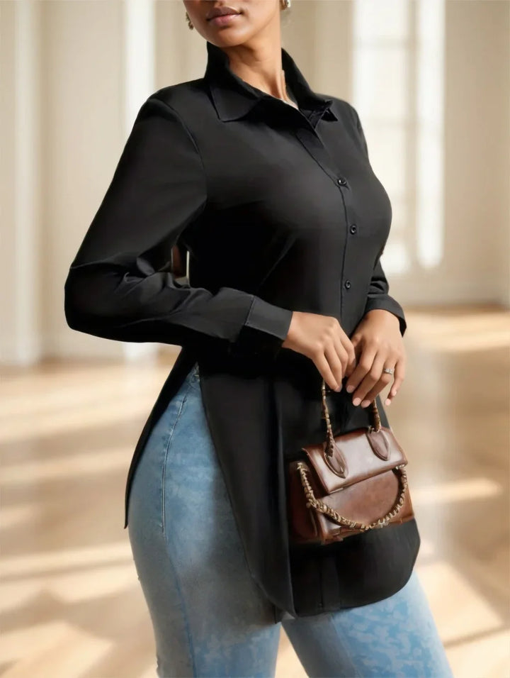 Woman wearing black button-up shirt and light blue jeans holding a small brown leather handbag indoors