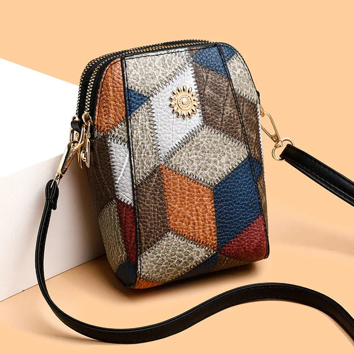 Colorful geometric patchwork leather crossbody bag with gold zipper and black strap on peach background