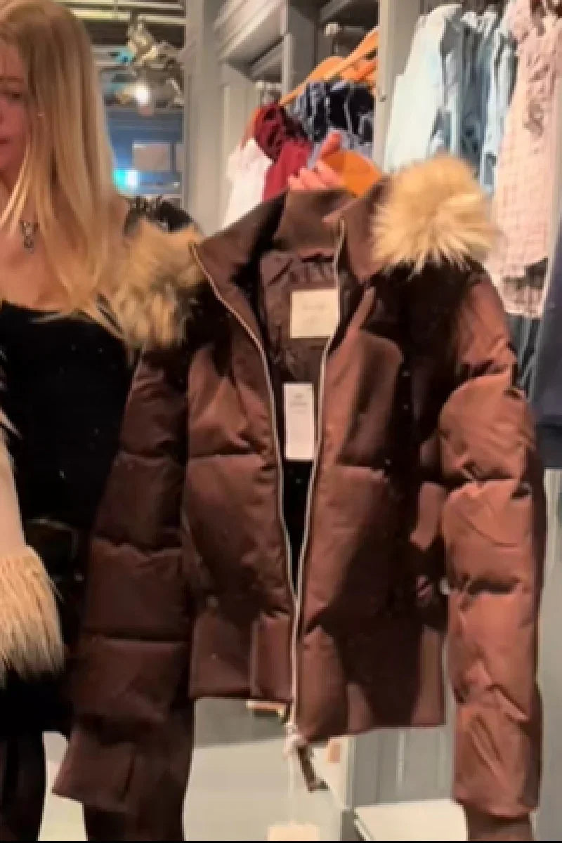 Brown puffer jacket with fur-lined hood on hanger in clothing store with woman nearby