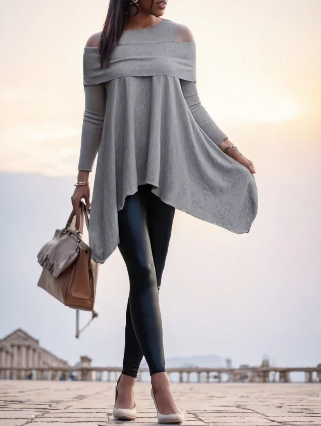 Woman in gray off-shoulder asymmetrical tunic with black leggings and beige heels holding brown handbag