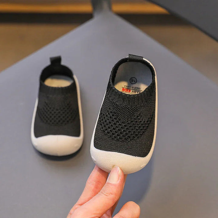 Black and white baby kids shoes with knit upper and flexible rubber sole on gray surface