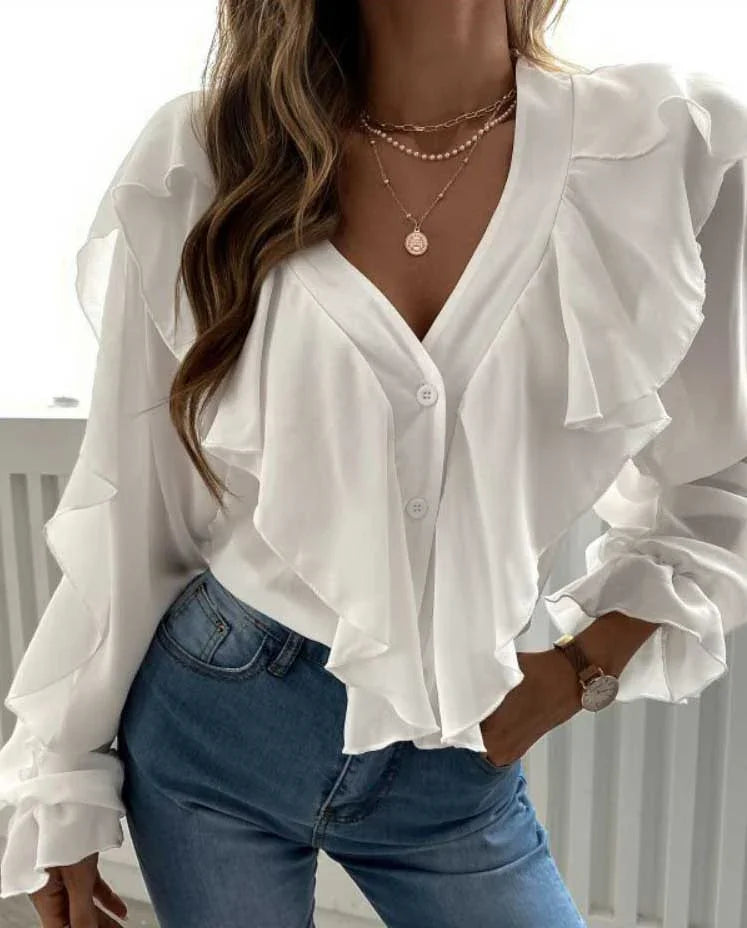 Woman wearing white ruffle-front blouse with v-neck and blue jeans, accessorized with layered gold necklaces and watch
