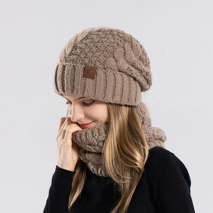 Woman wearing a beige knitted beanie and matching thick infinity scarf with cable knit pattern