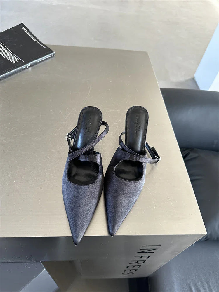 Elegant black pointed toe slingback heels with crisscross straps on a beige display table