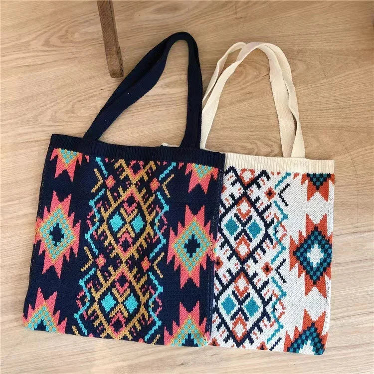 Two knitted tote bags with colorful geometric tribal patterns, one black and one white, on wooden floor
