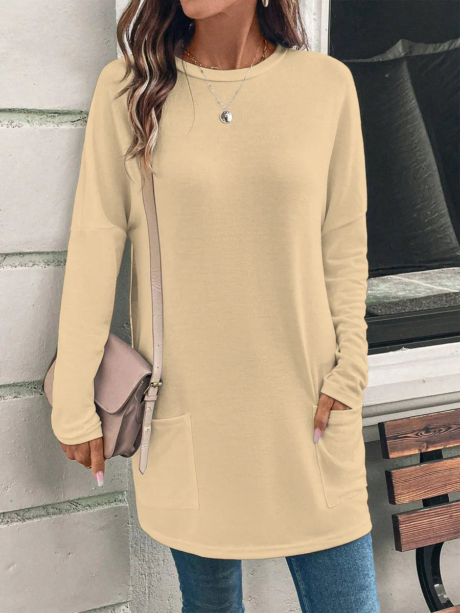 Woman wearing beige long sleeve tunic with pockets, blue jeans, necklace, and crossbody bag