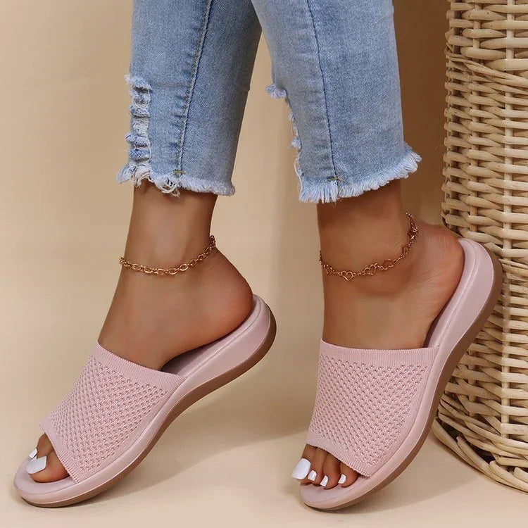 Woman wearing pink knitted slide sandals and light blue frayed hem jeans with gold ankle chain