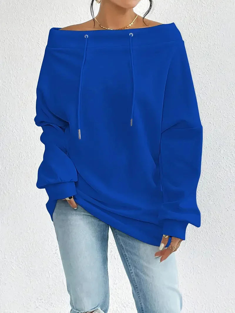 Woman wearing royal blue off-shoulder sweatshirt with drawstrings and light blue ripped jeans