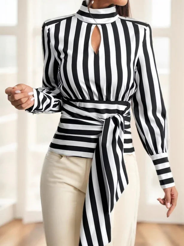 Woman wearing black and white vertical striped blouse with keyhole neckline and waist tie, paired with cream pants