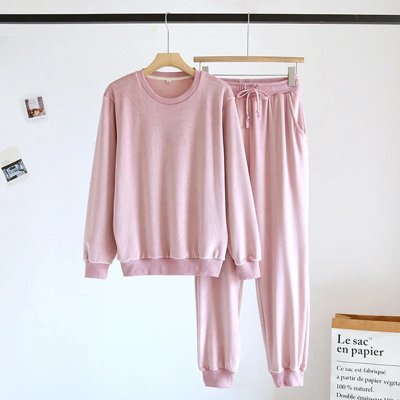 Soft pink fleece sweatshirt and jogger pants set hanging on wooden hangers against a white wall