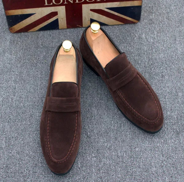 Pair of brown suede loafers with wooden shoe trees on gray carpet next to London Union Jack box