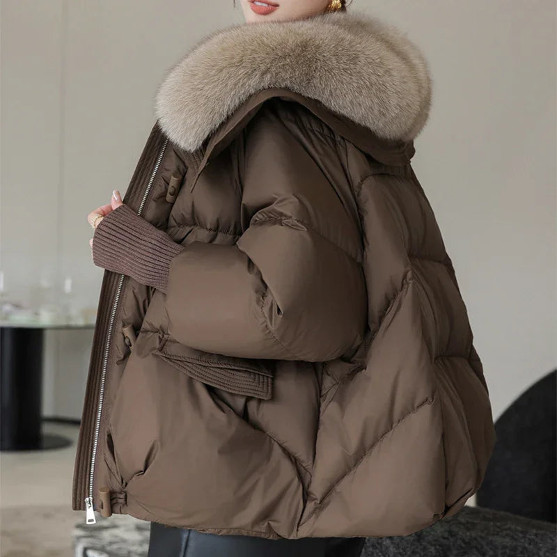 Woman wearing brown puffer jacket with large beige fur collar in modern indoor setting