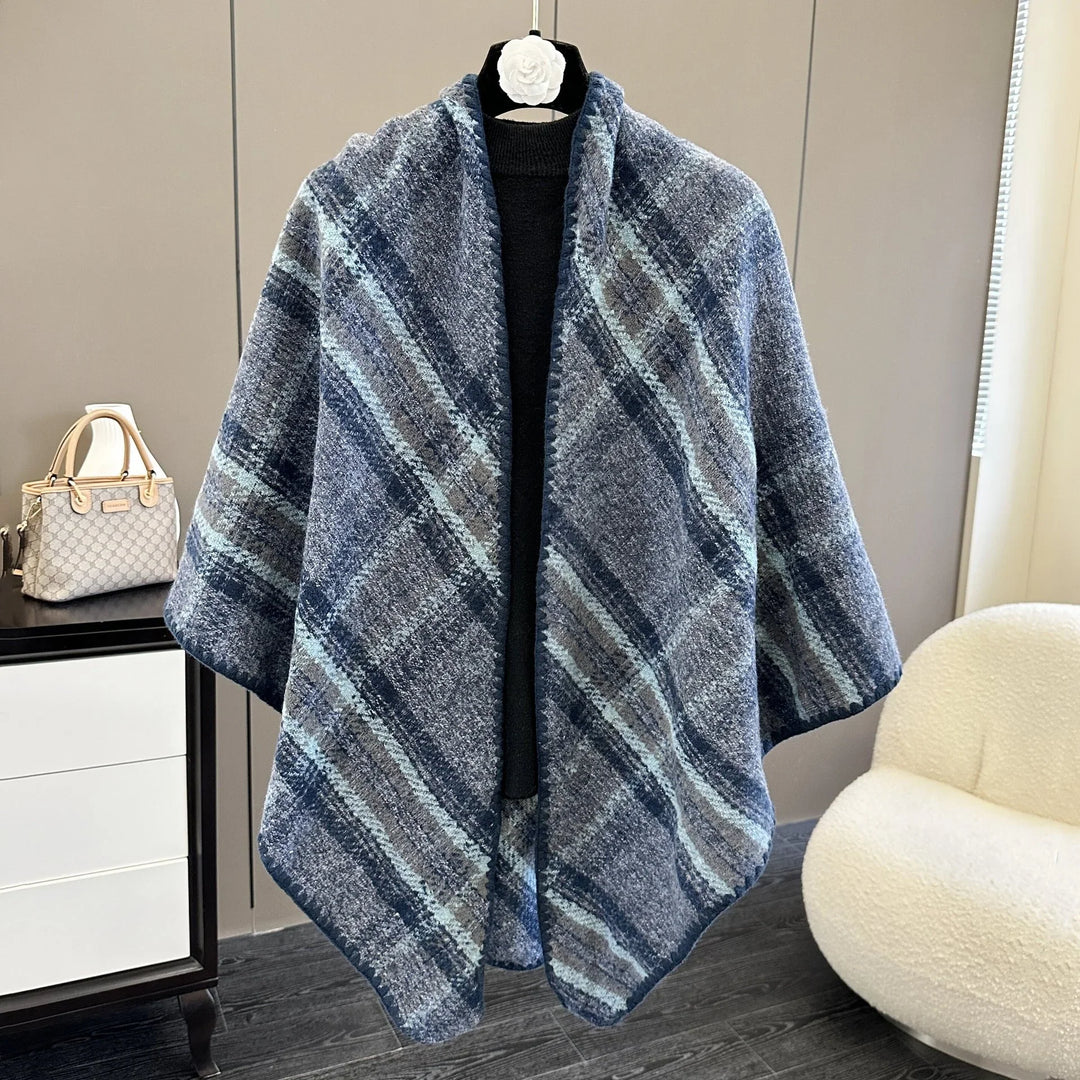 Blue and gray plaid wool poncho displayed on mannequin in modern room with handbag and white chair