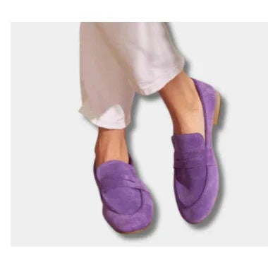 Person wearing purple suede loafers and light beige pants on a white background