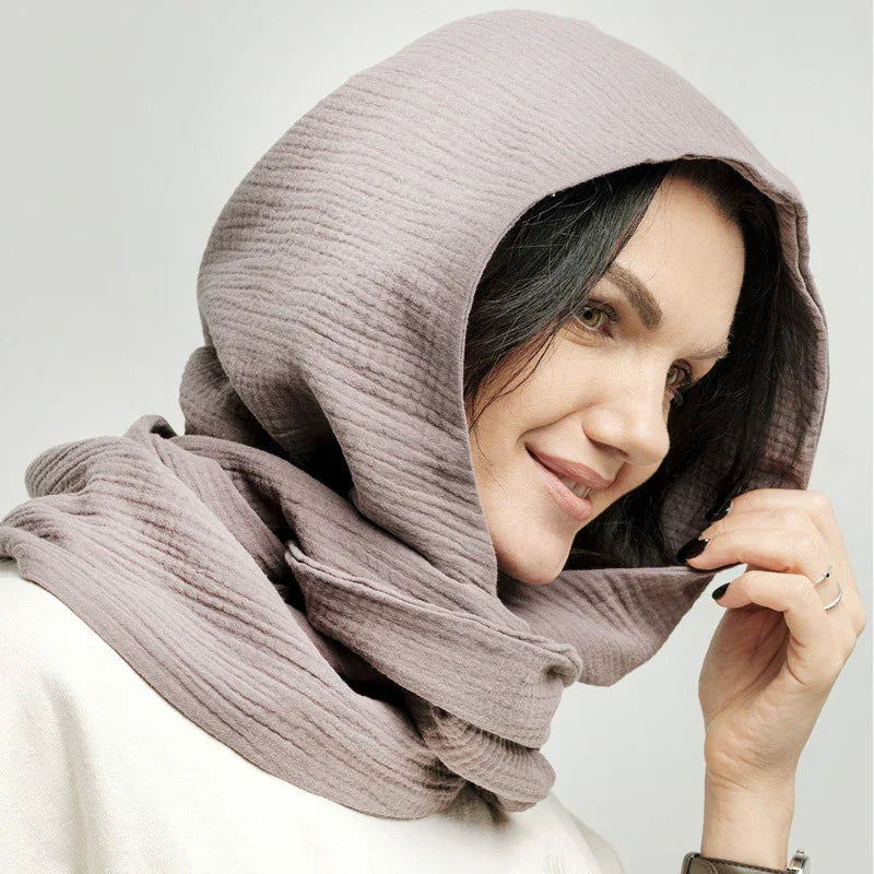 Smiling woman wearing textured light mauve hooded scarf and cream sweater, holding hood edge