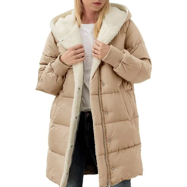 Woman wearing long beige puffer coat with white sherpa lining and hood, paired with white shirt and black jeans