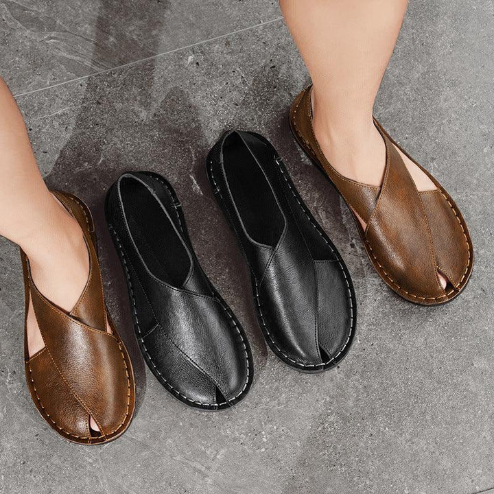 Pair of brown and black leather cross-strap slip-on sandals on gray stone floor