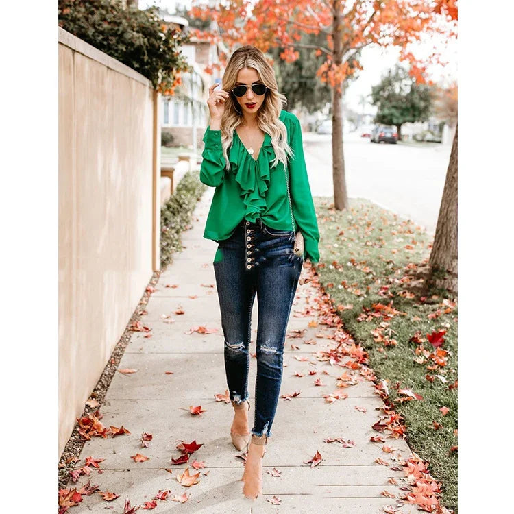 Woman wearing green ruffled blouse, high-waisted ripped skinny jeans, and sunglasses walking on autumn sidewalk
