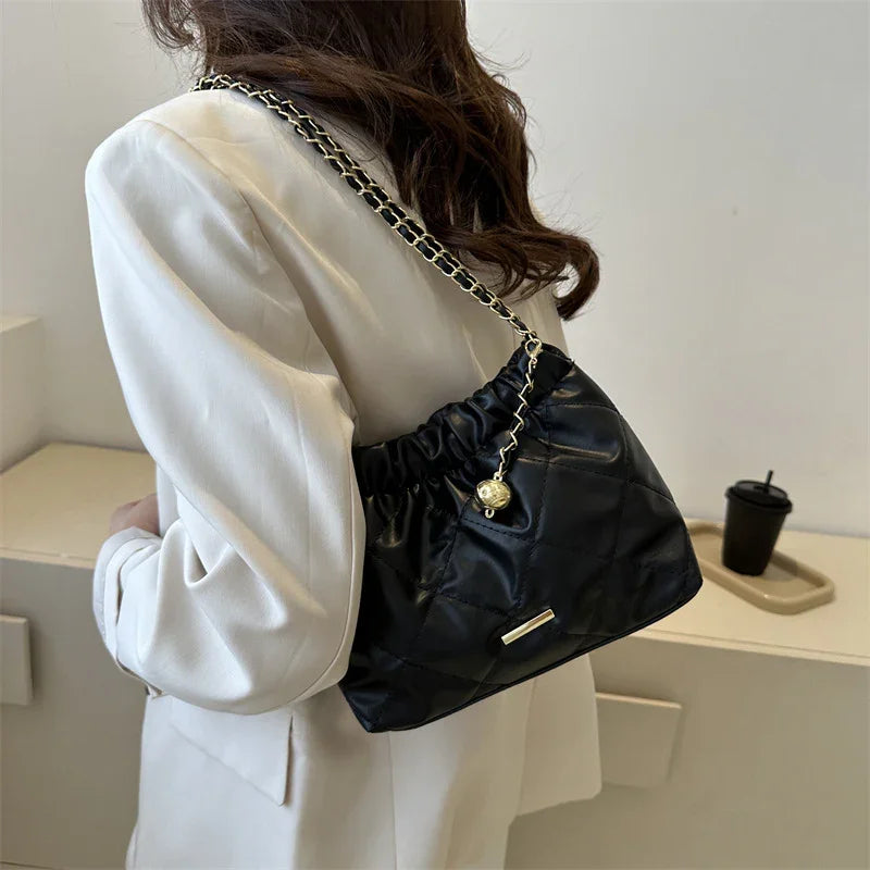 Woman wearing white blazer carrying black quilted leather shoulder bag with gold chain strap