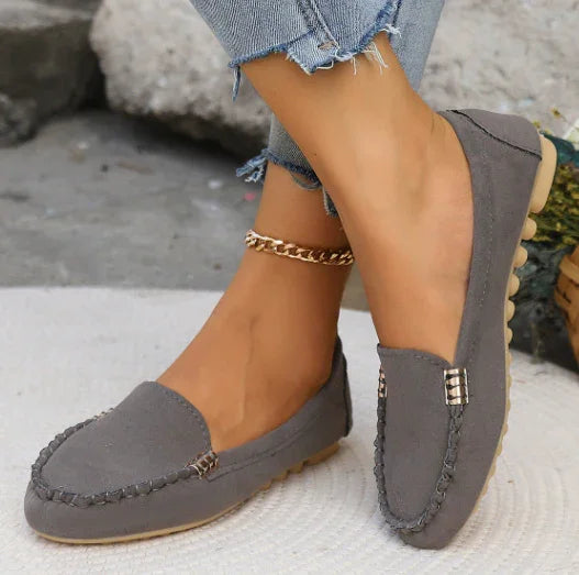 woman wearing grey casual loafers and frayed hem jeans on a light surface with stone background